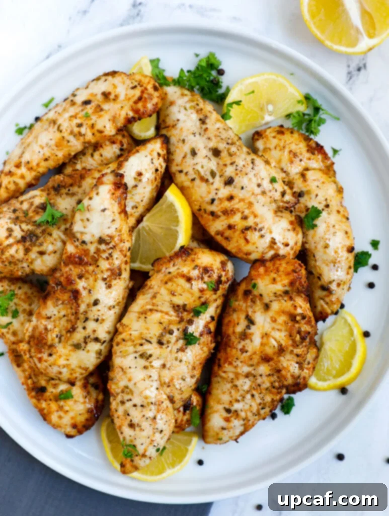 Top down view of perfectly cooked lemon pepper chicken tenders on a plate, garnished with fresh herbs and lemon wedges.