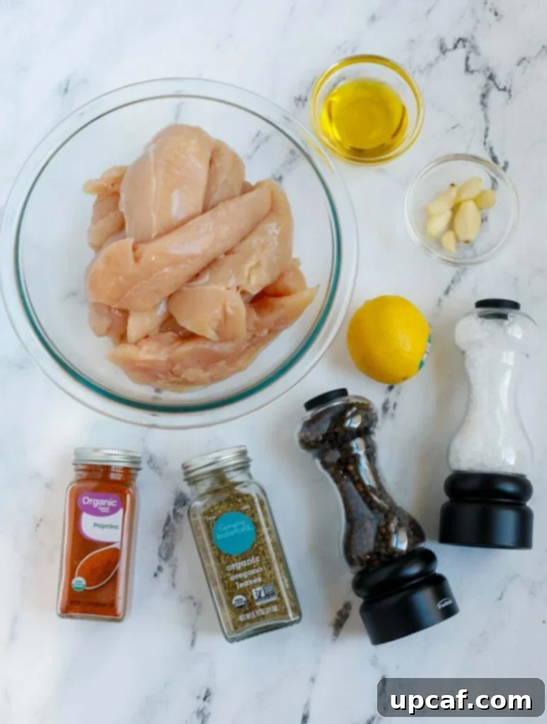 Top down view of ingredients for air fryer lemon pepper chicken recipe laid out on a cutting board, including chicken tenders, lemons, olive oil, and various spices.