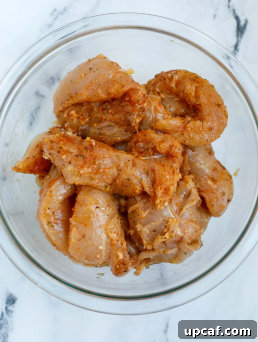Raw chicken tenders in a bowl, generously coated with the vibrant lemon pepper seasoning and marinade.