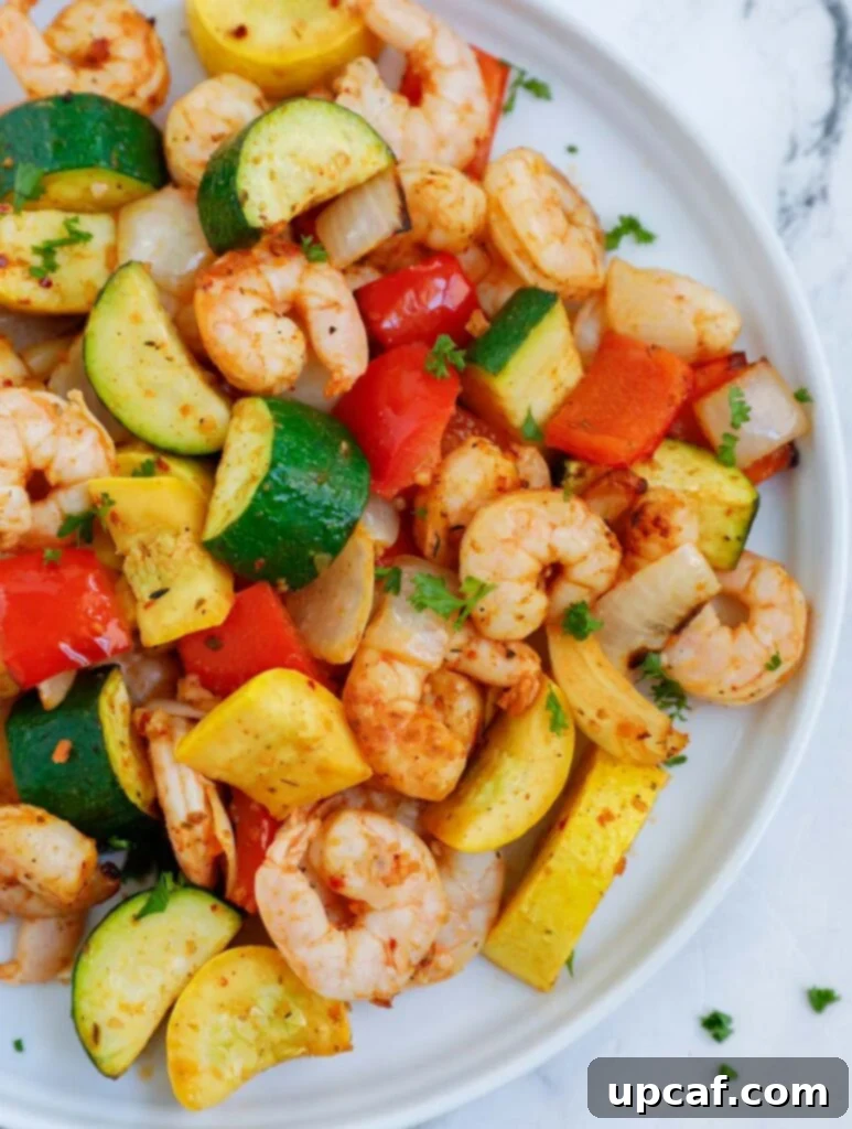 Top down shot of air fryer shrimp and vegetables beautifully arranged on a white plate, garnished with fresh herbs.