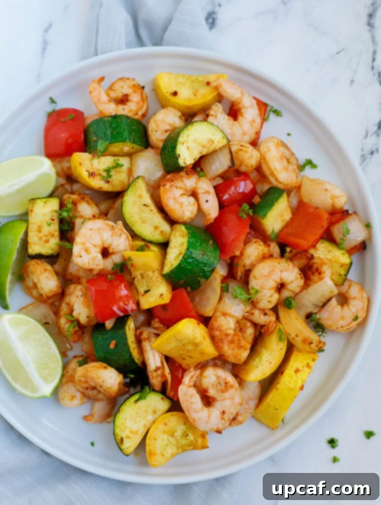 Top down shot of a generous serving of air fryer shrimp and vegetables on a pristine white plate, garnished with fresh herbs.