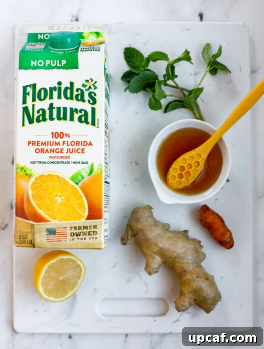 Top-down shot of all the fresh ingredients needed for the immune booster drink: Florida's Natural orange juice, ginger, turmeric, honey, and a lemon.