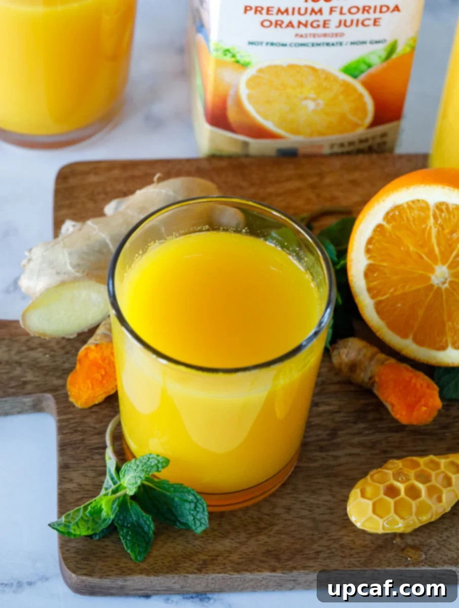 Orange booster drink surrounded by all its natural ingredients on a rustic wooden surface.