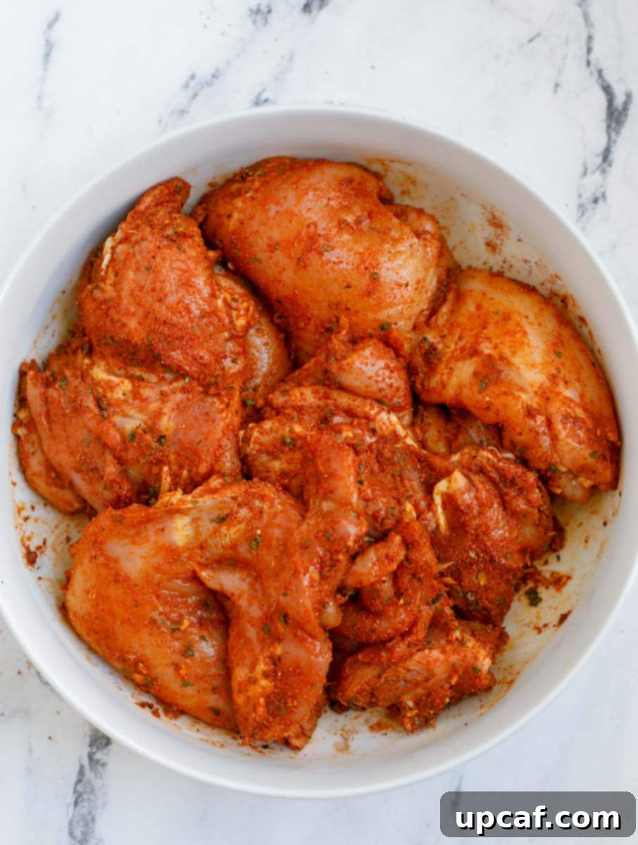 Crispy Juicy Air Fryer Boneless Thighs 5 Chicken thighs marinating in a bowl with spices and lemon.