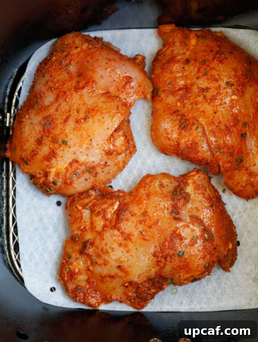 Crispy Juicy Air Fryer Boneless Thighs 6 Raw marinated chicken thighs arranged in a single layer in an air fryer basket, ready to cook.