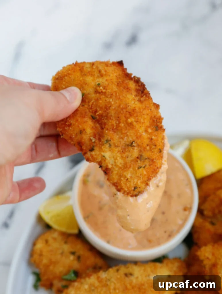 A crispy air fryer chicken strip being dipped into a bowl of special sauce.