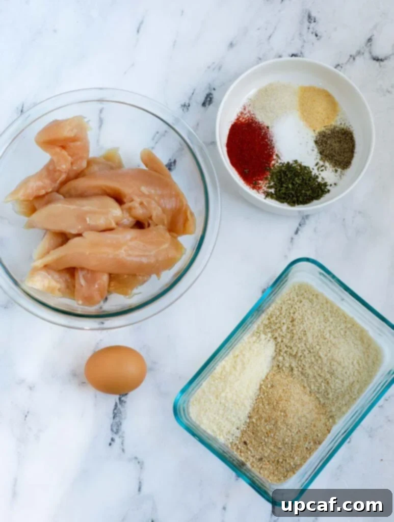 Arrangement of fresh ingredients for crispy air fryer chicken strips, including chicken, eggs, breadcrumbs, and spices.