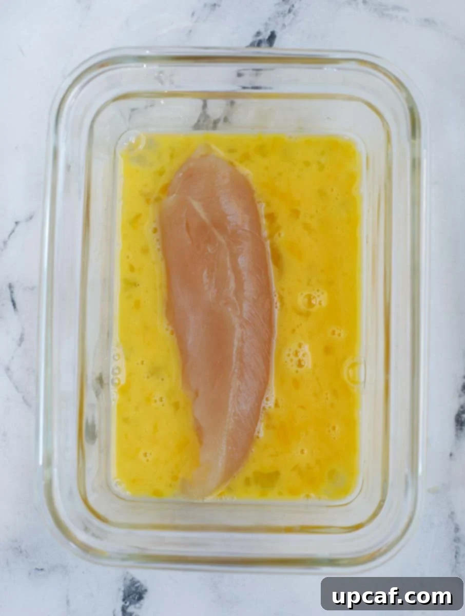 Chicken tender being dipped into an egg wash in a bowl.