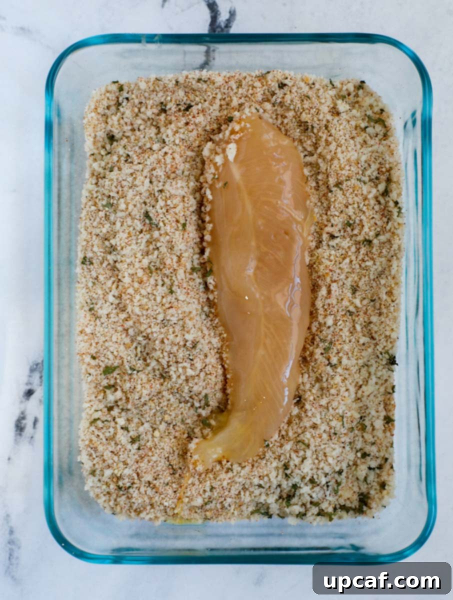 Chicken tender being coated in a seasoned breadcrumb mixture.