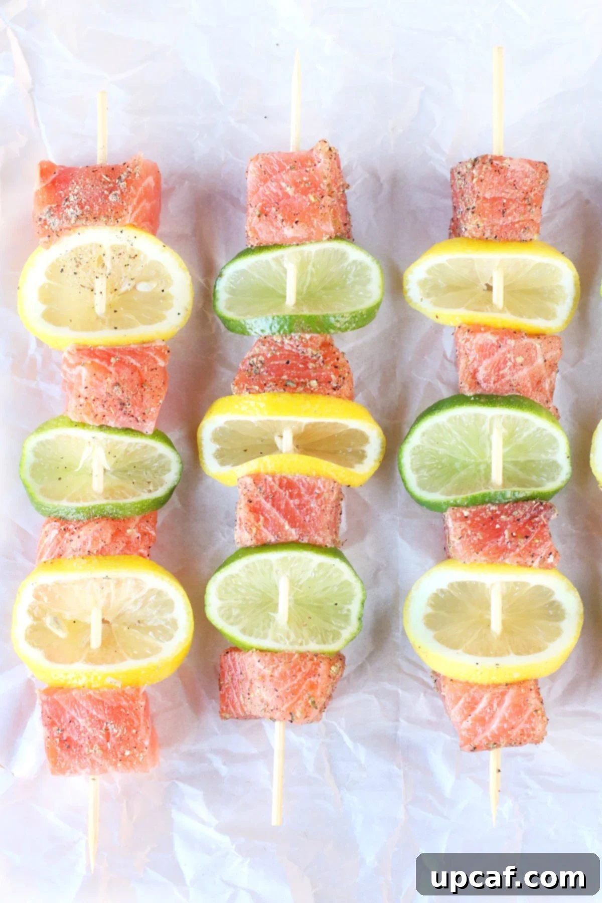 Zesty Salmon Kebabs 3 Fresh salmon skewers with lemon and lime laying on a lined pan ready to grill