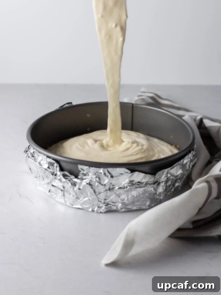 Cream cheese batter being poured into a prepared springform pan with a graham cracker crust.