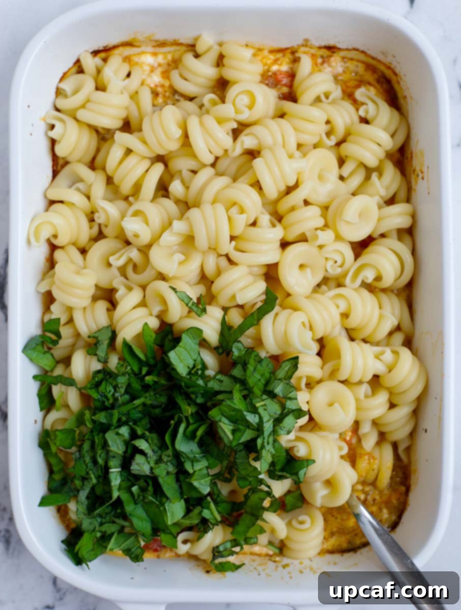 Golden Feta Pasta Bake 7 Adding cooked pasta and fresh basil to the feta and tomato sauce in a baking dish.