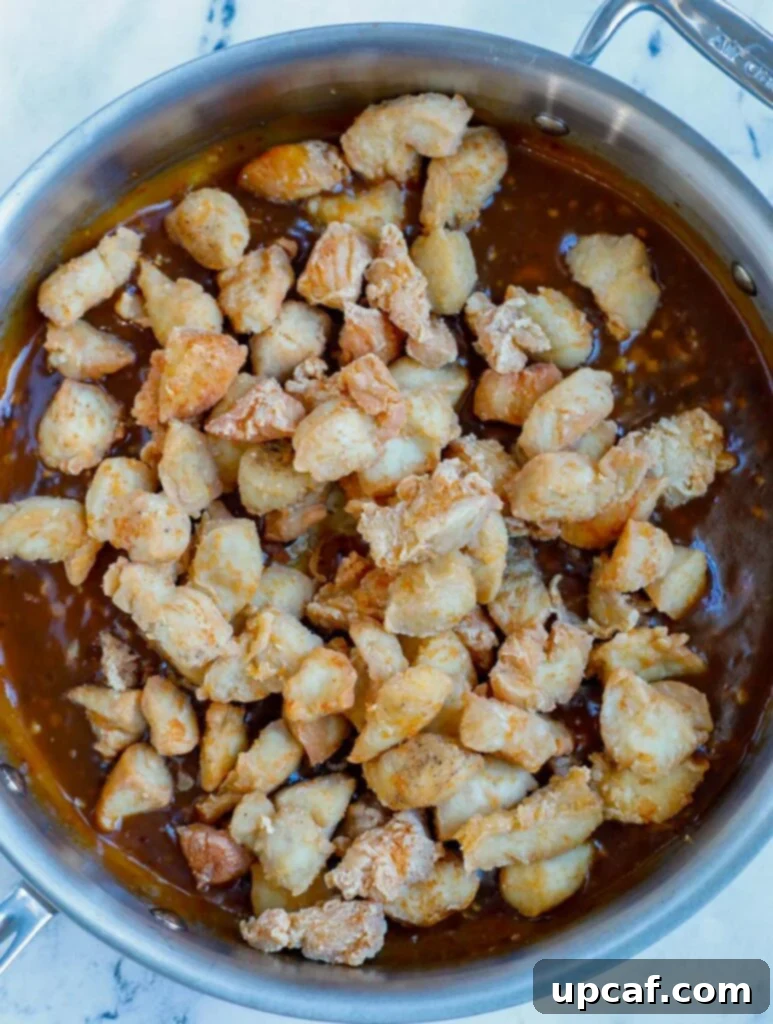 Chicken being added into the rich General Tso's sauce in a skillet.