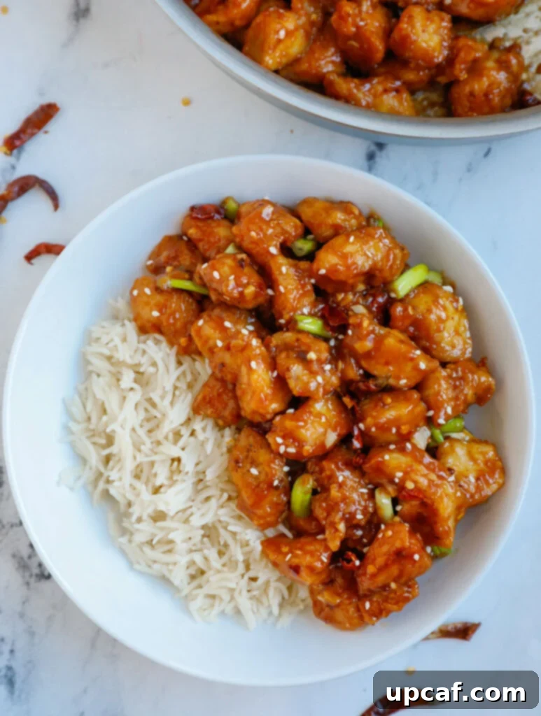 Overhead image of a bowl of General Tso's chicken with a side of white rice, garnished.