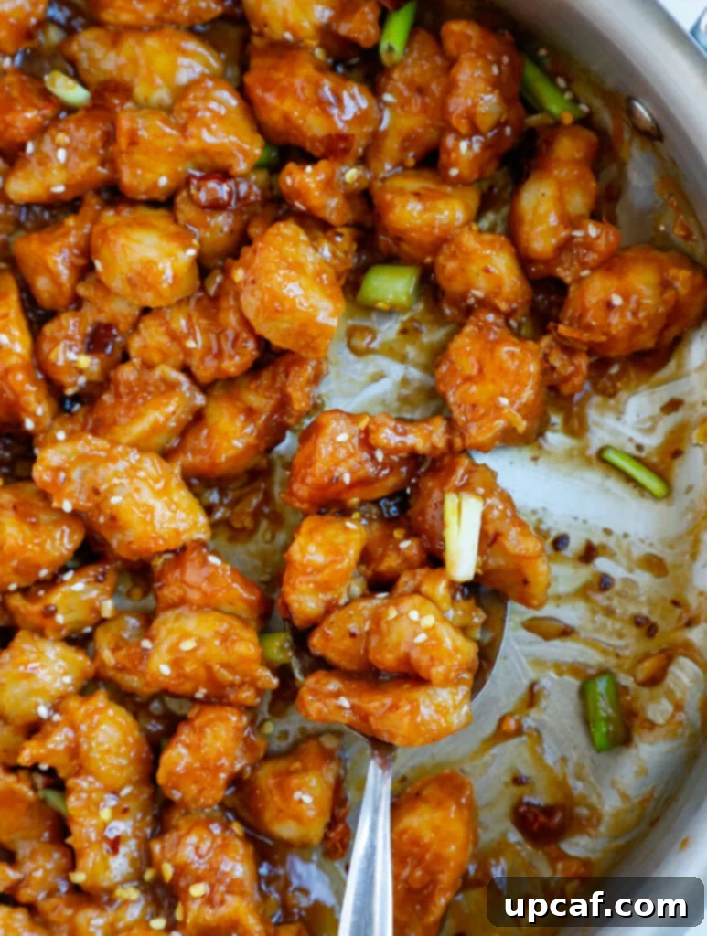 Close up of a spoonful of crispy General Tso's chicken, showcasing its glossy sauce.