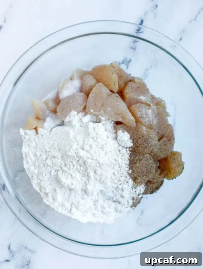 Chicken being added to a bowl with flour, salt, and pepper for coating.