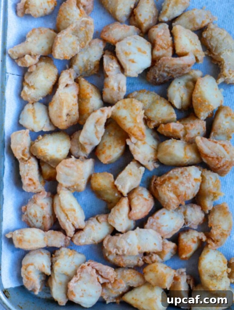 Cooked chicken pieces set aside on paper towels to drain excess oil after frying.