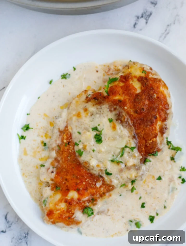 Extreme close-up of a crispy, golden-brown chicken breast topped with a generous amount of creamy Caesar sauce and melted Parmesan cheese, garnished with fresh herbs.
