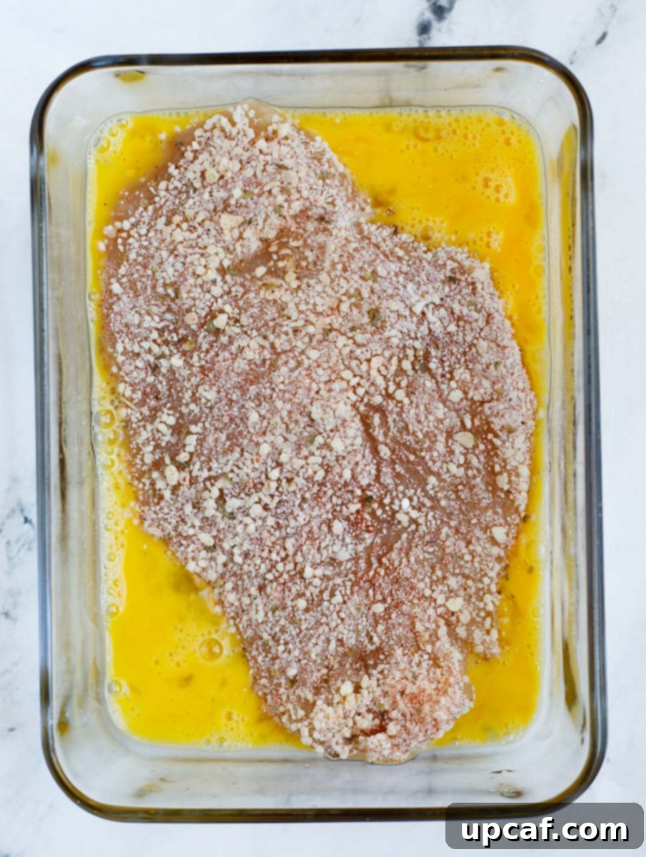 Chicken dredged in whisked egg wash, preparing for the dry coating.