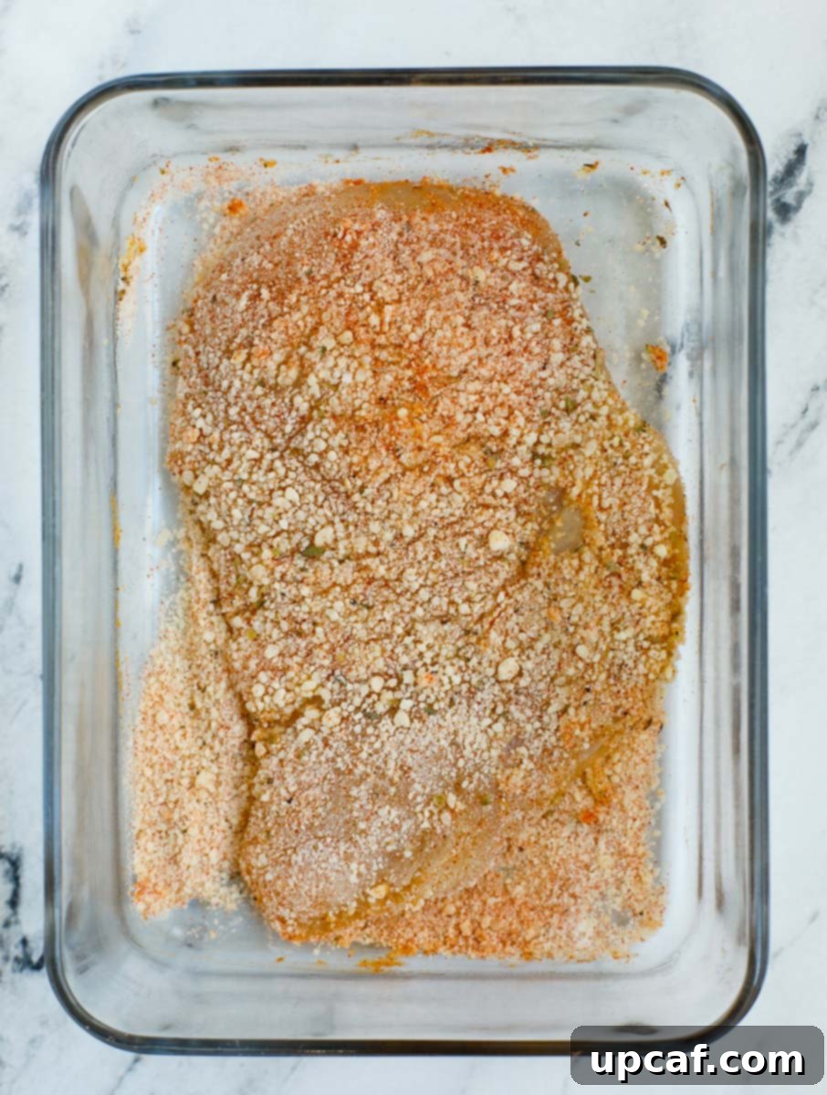 Egg-coated chicken being thoroughly covered with the seasoned flour and Parmesan mixture.