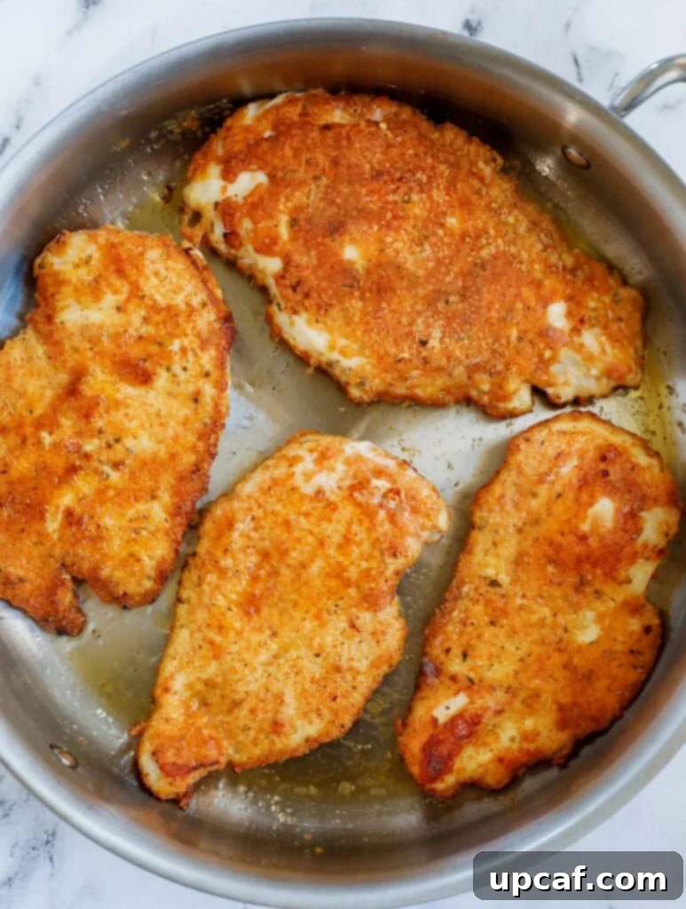 Golden-brown, pan-fried chicken breasts sizzling in an oven-safe skillet, ready for sauce.