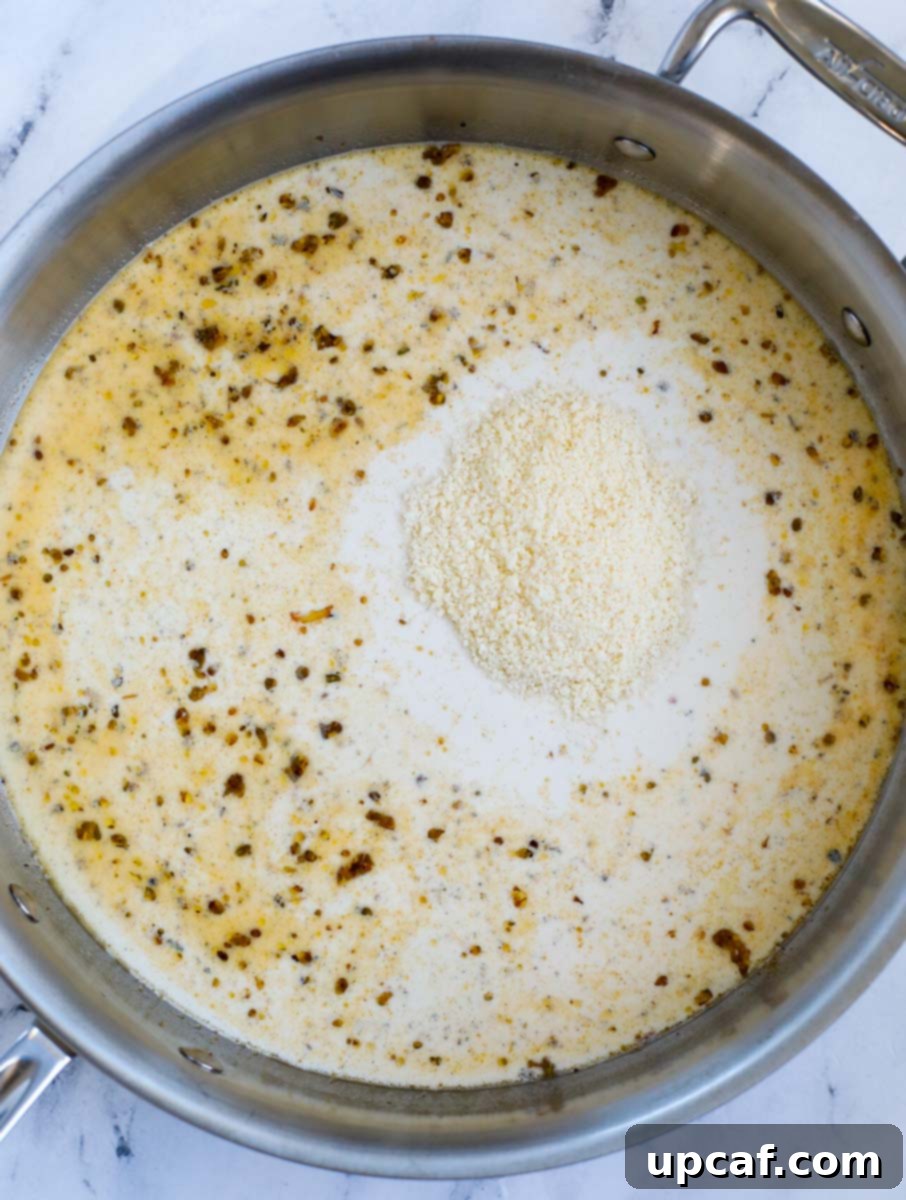 Grated Parmesan cheese being stirred into the simmering creamy sauce in a skillet.