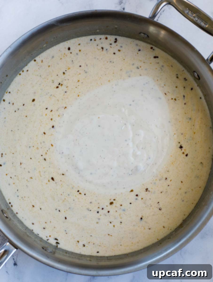 Half and half being poured into the skillet with garlic and spices, forming the base of the creamy sauce.