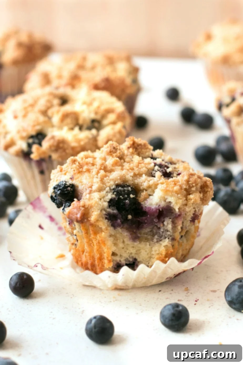 Blueberry crumb muffins sitting on a white surface with one having a bite taken from it