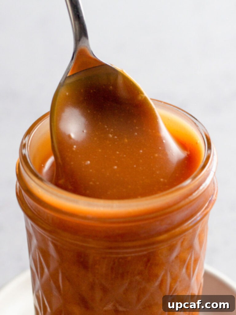 Close up of homemade caramel sauce in a jar with a spoon, ready to be served over desserts.