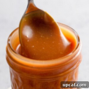 Close up of caramel sauce in a jar with a spoon.