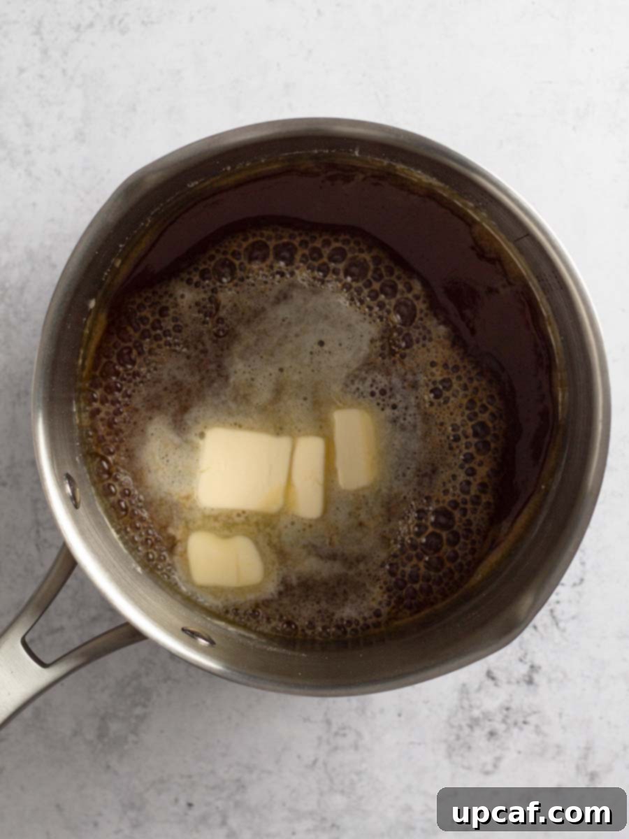Small pieces of unsalted butter being added to the hot, caramelized sugar in the saucepan, causing it to bubble and sizzle.