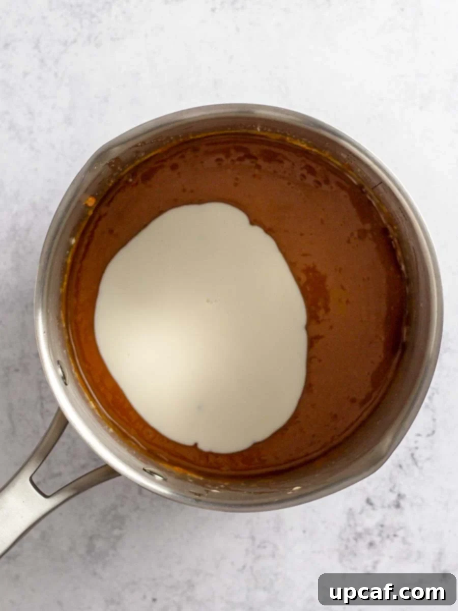Heavy cream being slowly poured into the bubbling caramel and butter mixture, while continuously whisking.