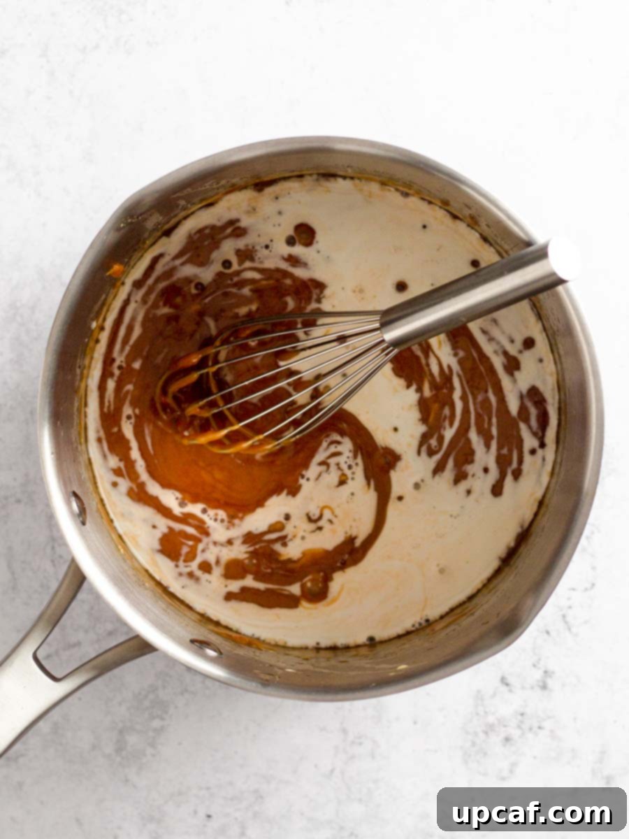 The caramel sauce being vigorously whisked in the saucepan, achieving a smooth and homogenous consistency after all ingredients are added.