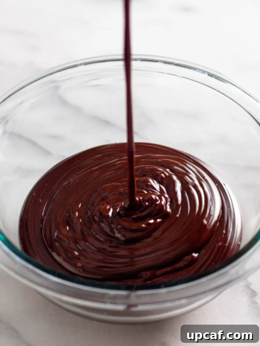 Smooth, rich chocolate ganache being poured in a steady stream into a clean bowl, showcasing its glossy texture.