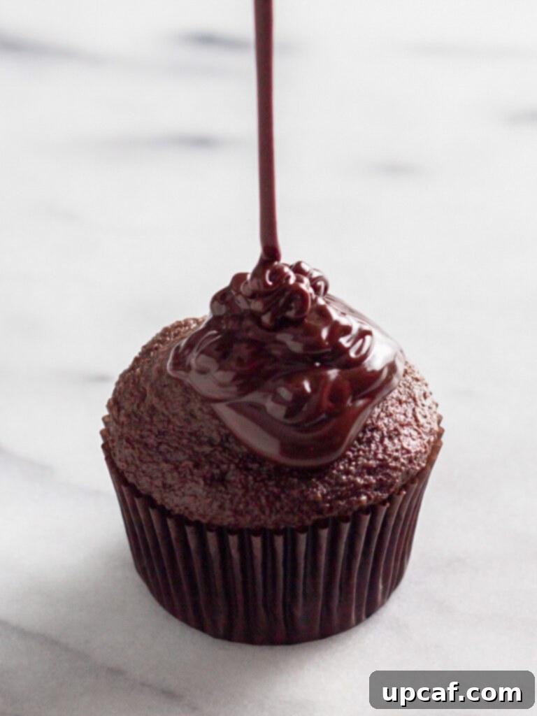 A delectable cupcake generously covered with a glossy, smooth chocolate ganache, highlighting its rich texture and shine.