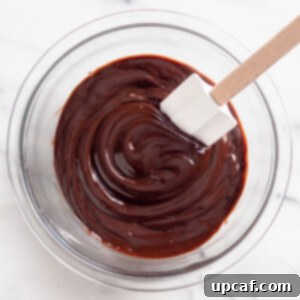 Mixing chocolate ganache in a bowl with a spatula, showcasing its smooth texture.