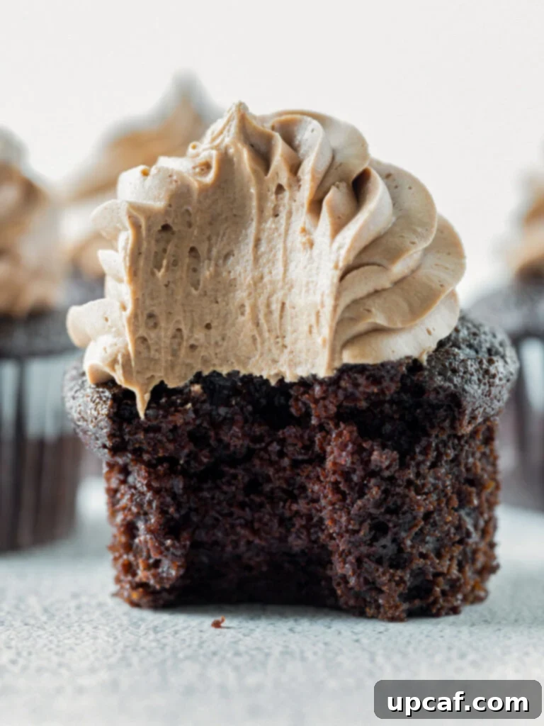 Close-up shot of a perfectly frosted chocolate cupcake with a bite taken out, revealing its moist, dark chocolate interior.