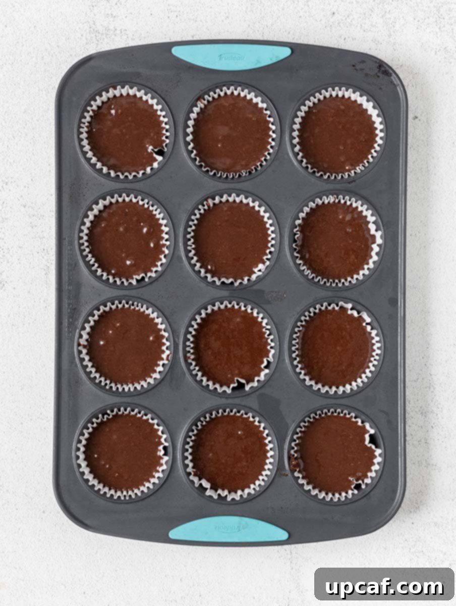 Muffin pan filled with chocolate cupcake batter in liners, ready for the oven.
