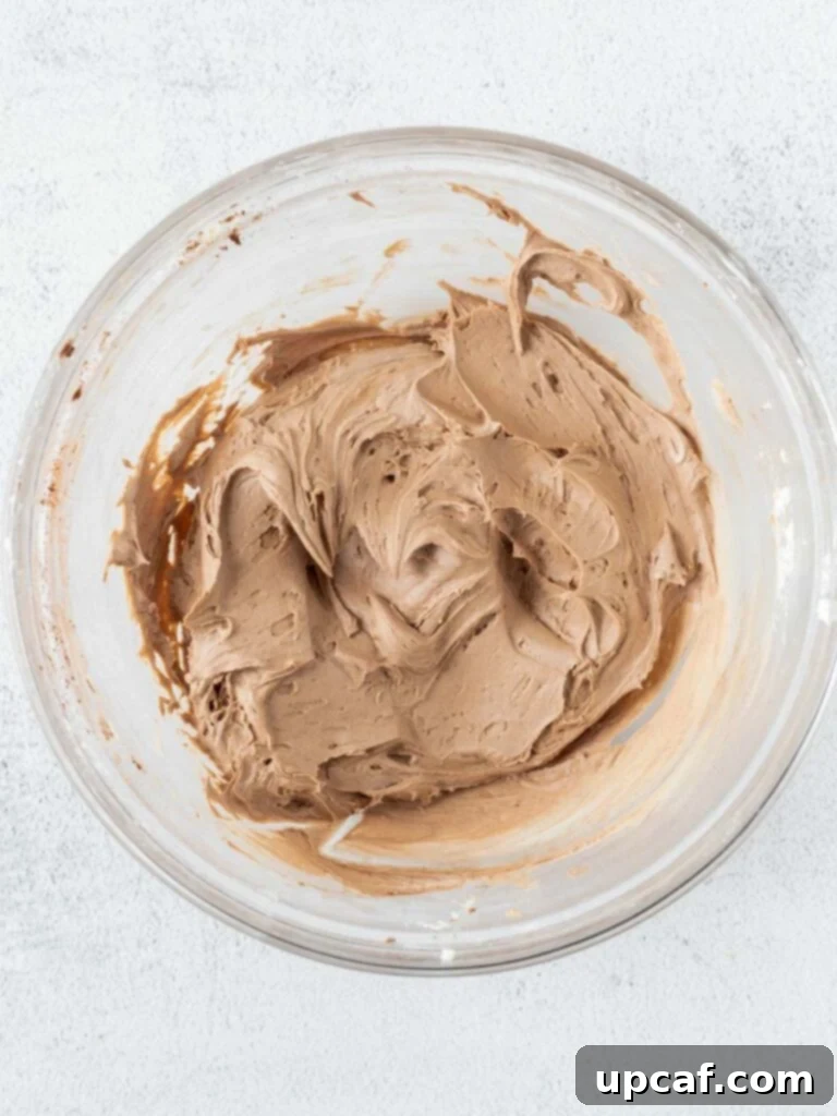 Rich, glossy chocolate frosting in a mixing bowl, ready to be piped onto cupcakes.