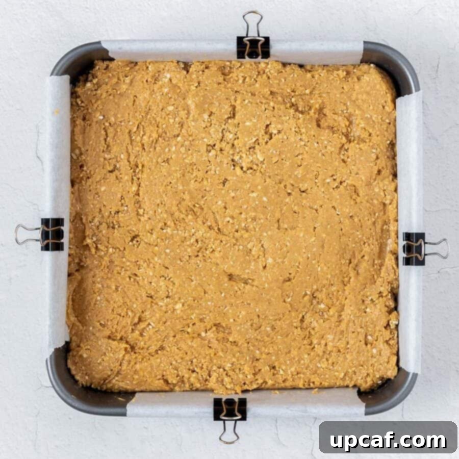 Top-down shot of the peanut butter oat mixture pressed evenly into a square pan.
