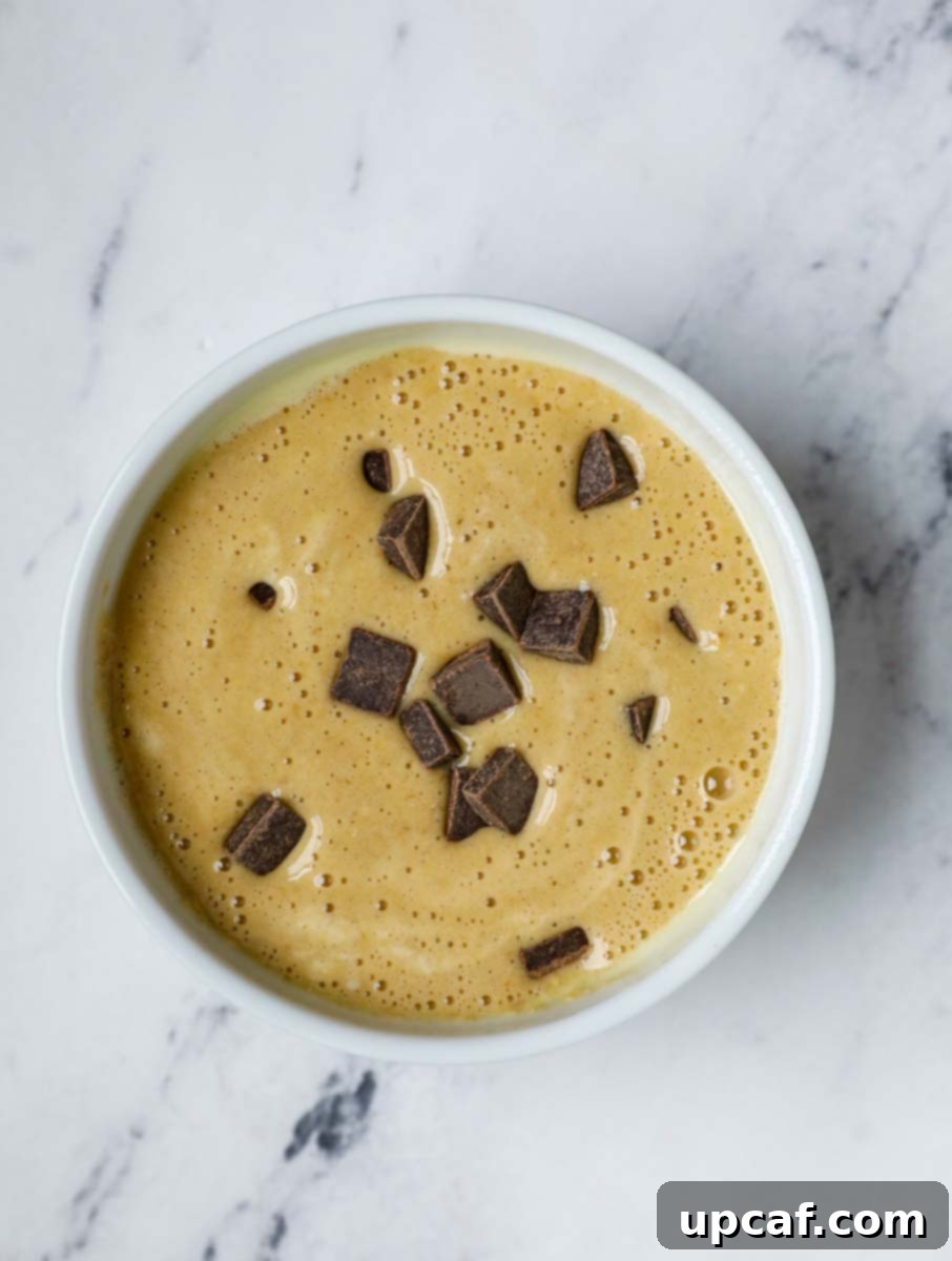 Chocolate chips being added to banana baked oats batter in a ramekin.