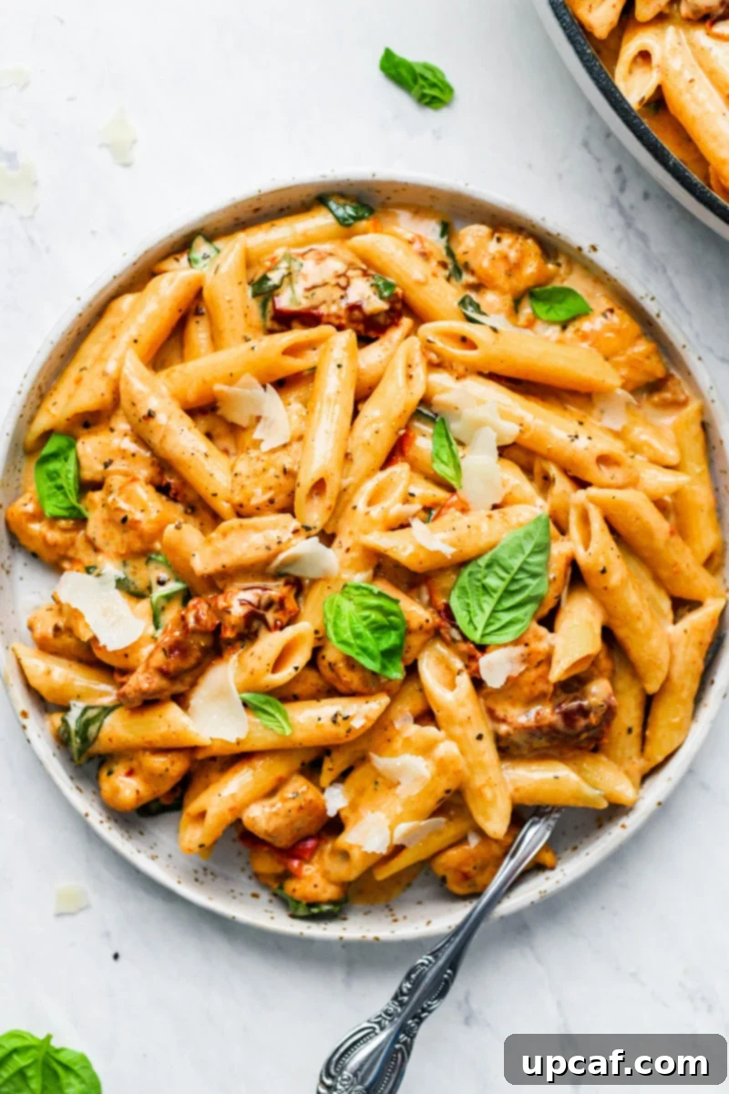 A plate of creamy sun-dried tomato pasta with fresh basil and parmesan shavings on top. The dish is rich and inviting, ready to be served.