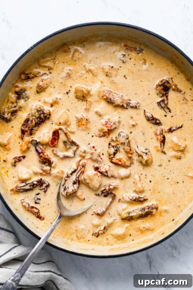 Sauce being made in a pot for sun-dried tomato pasta. Garlic and sun-dried tomatoes are simmering in a creamy base.