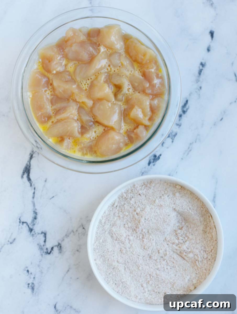 Wholesome Orange Chicken 4 Cubed chicken soaking in an egg mixture, alongside a bowl containing the dry breading ingredients.