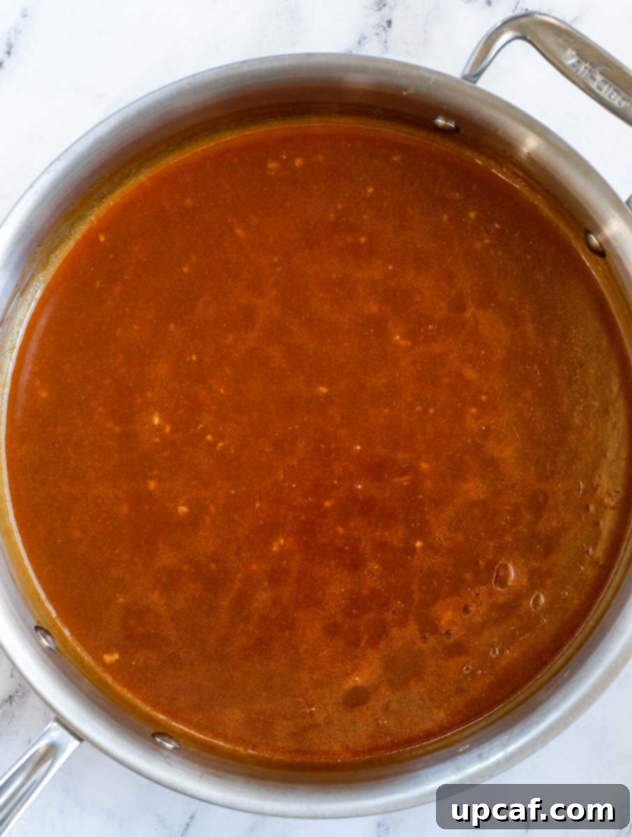 Wholesome Orange Chicken 7 The healthy orange chicken sauce simmering and thickening in a pan on the stovetop.