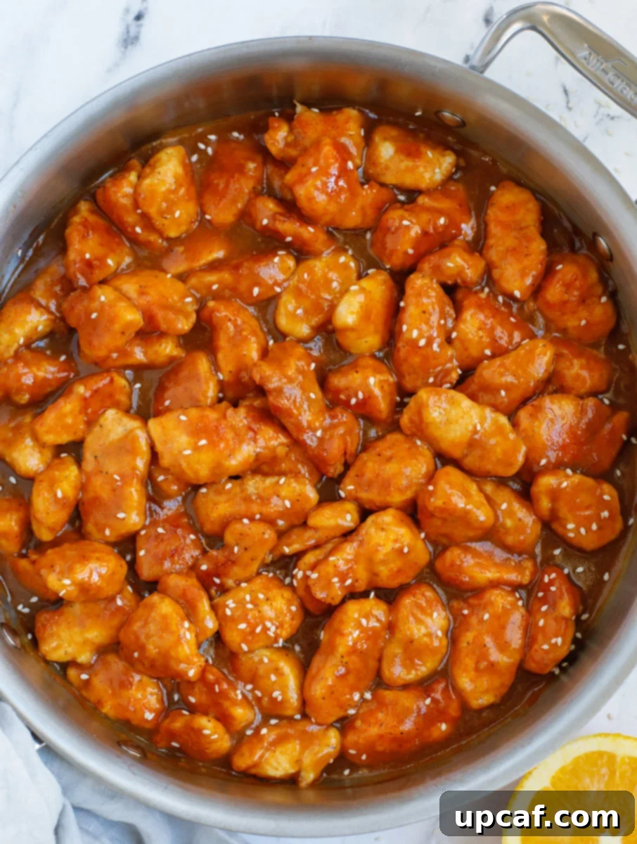 Wholesome Orange Chicken 9 Healthy baked orange chicken, generously coated in sauce, glistening in a pan.