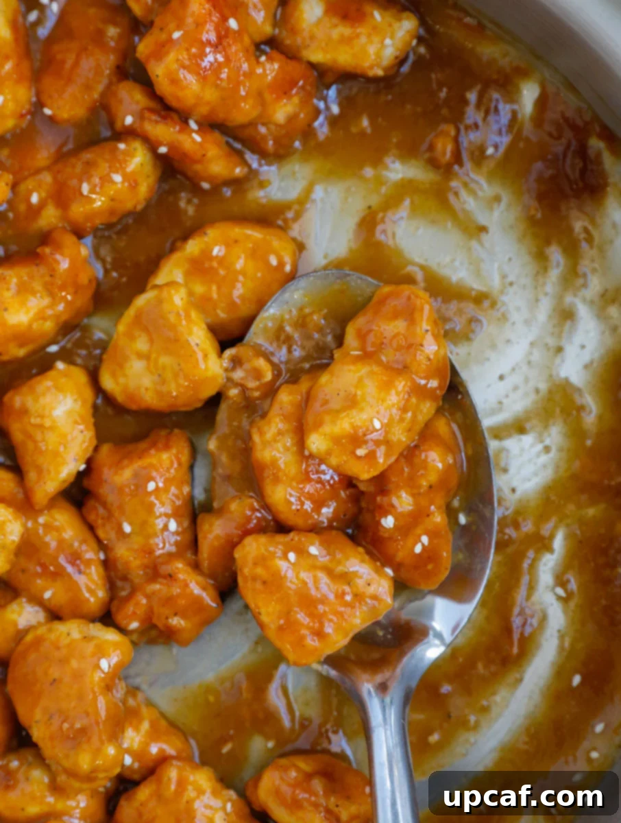 Wholesome Orange Chicken 10 A close-up of a spoonful of glistening healthy orange chicken, coated in sauce and ready to be enjoyed.