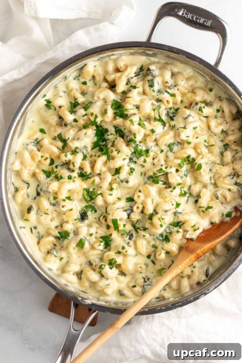 Top-down shot of creamy spinach mac and cheese in a rustic skillet with a wooden spoon, garnished with fresh parsley.