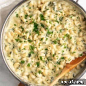 Top down shot of spinach mac and cheese with wooden spoon in skillet