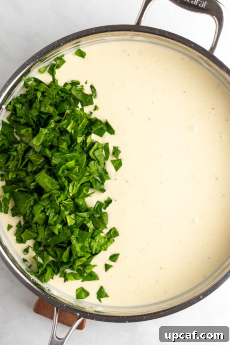 Fresh spinach wilting into the hot, creamy cheese sauce in a skillet.